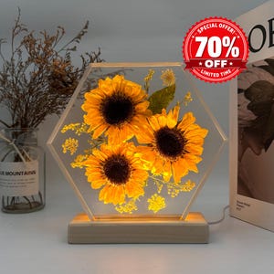 May include: A hexagonal clear resin lamp featuring three pressed yellow sunflowers and small green foliage, set on a light wood base. A red circular sticker in the top right corner displays the text 70% OFF LIMITED TIME.