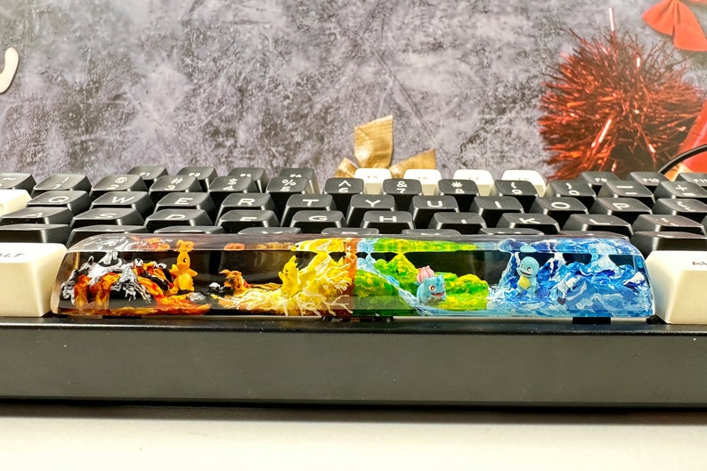 May include: A keyboard with a colorful resin keycap featuring a Pokemon theme. The keycap is divided into four sections, each with a different color and Pokemon character. The first section is orange and features a Charmander, the second is yellow and features a Pikachu, the third is green and features a Bulbasaur, and the fourth is blue and features a Squirtle.