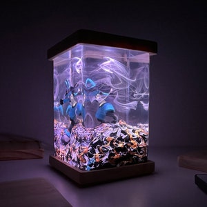 May include: A clear resin lamp with a wooden base. The resin contains blue and black figurines and swirling white smoke-like patterns. The base is a dark brown wood.