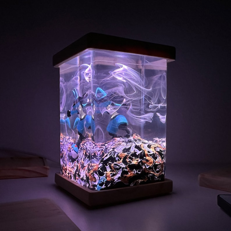 May include: A clear resin lamp with a wooden base. The resin contains blue and black figurines and swirling white smoke-like patterns. The base is a dark brown wood.