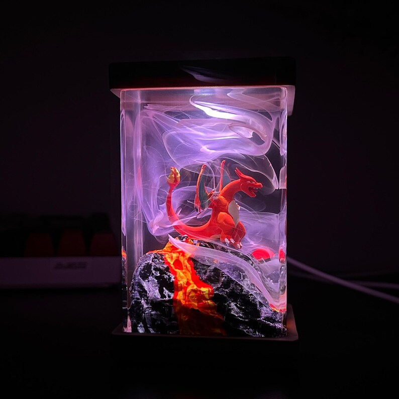 K&ouml;nnte beinhalten: Eine rote Drachenfigur in einem durchsichtigen Glasw&uuml;rfel mit einem wirbelnden wei&szlig;en Raucheffekt und einem lavaartigen Sockel.