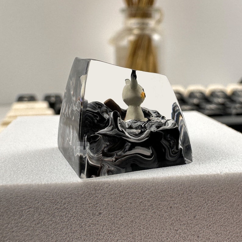 K&ouml;nnte beinhalten: Ein transparenter Harz-Tastenkappen mit einem schwarzen und wei&szlig;en Wirbelmuster. Eine kleine wei&szlig;e Figur eines Katzes befindet sich im Inneren der Tastenkappe.