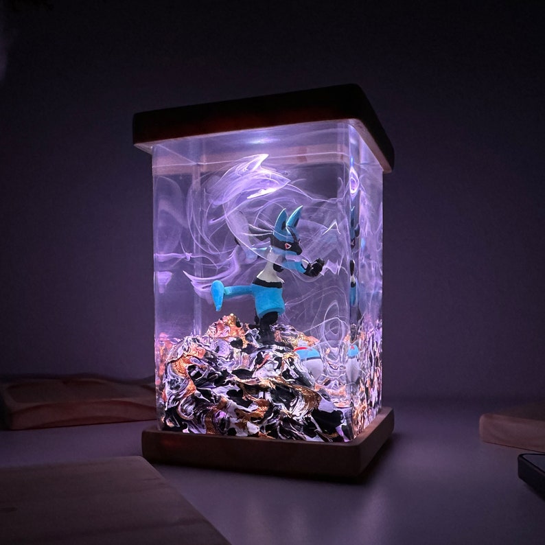 May include: A blue and white Pokemon figurine is encased in a clear resin cube with a wooden base. The cube is illuminated from within, creating a glowing effect. The resin contains swirling white and gold accents.