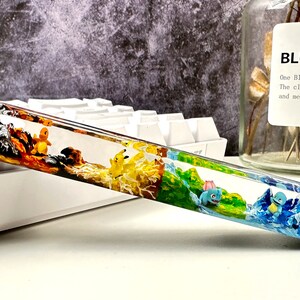 May include: A clear resin keyboard wrist rest with four different colored sections, each featuring a different Pokemon character. The sections are orange, yellow, green, and blue.