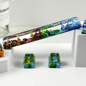 May include: Five colorful resin keycaps with different Pokemon characters. The keycaps are on a white surface. The keycaps are made of clear resin with different colored layers. The keycaps are all different sizes and shapes. The keycaps are all different colors. The keycaps are all different designs.