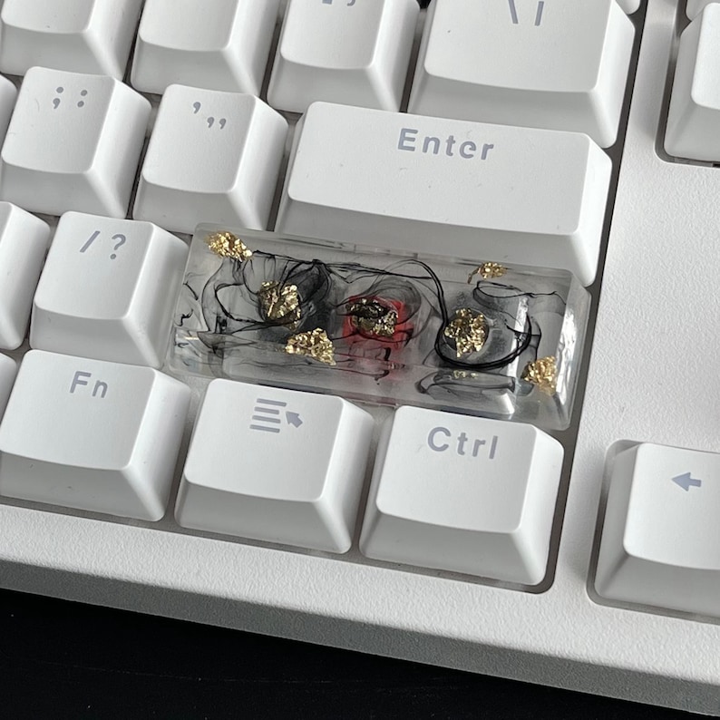 K&ouml;nnte beinhalten: Eine transparente Harz-Tastenkappe mit schwarzen Wirbeln, goldenen Flocken und roten und silbernen Akzenten. Die Tastenkappe ist f&uuml;r eine Standard-mechanische Tastatur ausgelegt.