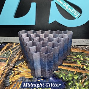 May include: A 3D-printed, hexagonal-shaped Midnight Glitter organizer. The organizer is a gradient of dark blue to silver with glitter. The text "Midnight Glitter" is displayed on the bottom of the image. The text "Zodiac Shadows Only on Etsy" is also visible.