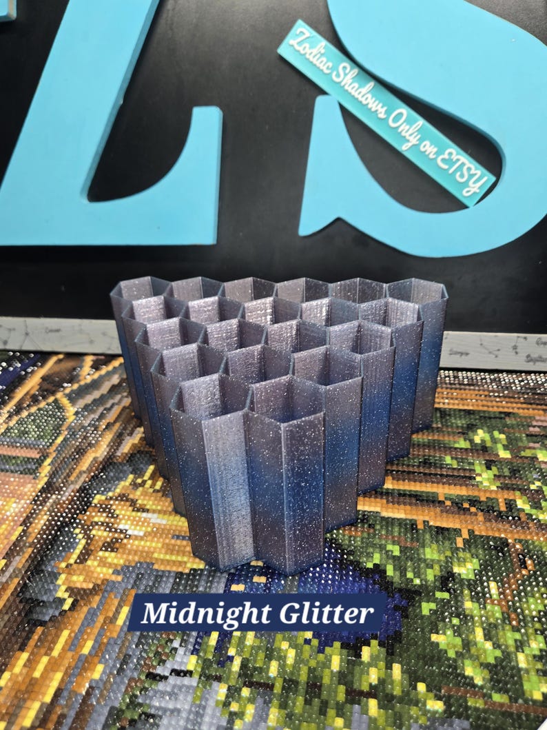 May include: A 3D-printed, hexagonal-shaped Midnight Glitter organizer. The organizer is a gradient of dark blue to silver with glitter. The text "Midnight Glitter" is displayed on the bottom of the image. The text "Zodiac Shadows Only on Etsy" is also visible.