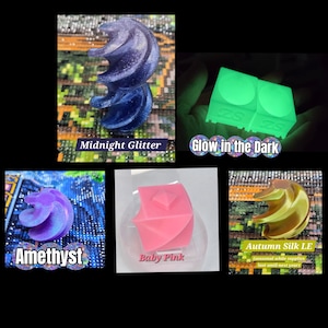 May include: A collection of five small, three-dimensional objects in various shapes and colours. Included are a dark blue glitter spiral, a glowing green cube, a purple spiral, a solid baby pink cube, and a metallic gold spiral.