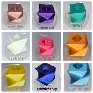 May include: A collection of nine 3D-printed geometric sculptures in various colors, including rose gold, purple, mint, white, pink, orange, yellow, midnight sky, and bright blue. Each sculpture has a unique, layered design with a pyramid on top, and is displayed on a clear stand.