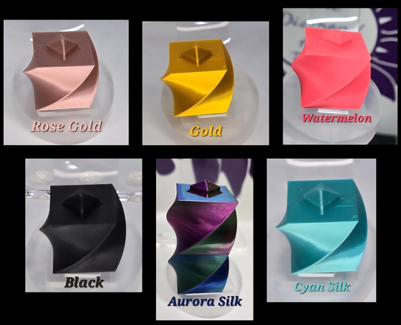 May include: A collection of six 3D printed geometric cube objects with a twisted design and a small pyramid on top. The colours include rose gold, gold, watermelon pink, matte black, iridescent aurora silk, and cyan silk, each labelled with its colour name.