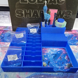 May include: A blue plastic diamond painting organiser tray with multiple compartments, holding small bags of blue resin drills, a black marker, a blue flower-topped stylus, a pink tube, and a square image of a whale in a vibrant underwater scene.
