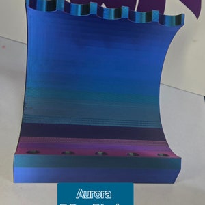 May include: A 5 pen display made of iridescent blue, green, and purple plastic. The display has a curved shape and a textured surface. The text "Aurora 5 Pen Display" is printed on the front of the display.