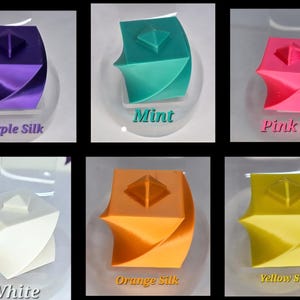 May include: Six small cube-shaped objects with a twisted design and a pyramid top, displayed in purple silk, mint, pink silk, white, orange silk, and yellow silk colours. Each cube features a smooth finish and is labelled with its respective colour name.