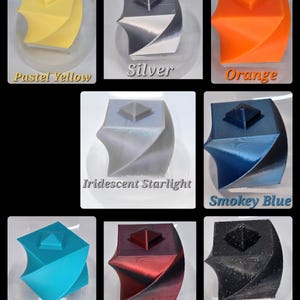 May include: A collection of eight square-based, twisted geometric objects with a small pyramid topper, displayed in various colours including pastel yellow, silver, orange, iridescent starlight, smokey blue, tiffany blue, red nebula silk, and black glitter.