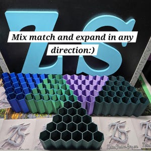 May include: A collection of colorful, honeycomb-shaped storage units in blue, green, purple, and dark green. The units are arranged in a display with the text "Mix match and expand in any direction:)" above them. A large, light blue "ZS" logo is in the background.
