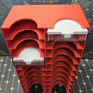 Może przedstawiać: Czerwona plastikowa skrzynka do przechowywania z wieloma przegródkami do organizowania drobnych przedmiotów. Skrzynka ma przezroczystą plastikową pokrywę z białym wkładem.