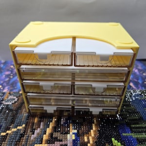 May include: A yellow plastic six-drawer organizer with clear plastic drawers. The organizer is ideal for storing small items like beads, buttons, or jewelry.