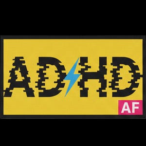 Könnte beinhalten: Ein rechteckiger gelber Aufnäher mit schwarzem Rand, der den Text ADHD in einer Glitch-Schriftart zeigt. Ein hellblauer Blitz ersetzt den Buchstaben H. In der unteren rechten Ecke befindet sich ein kleines rosa Rechteck mit dem weißen Text AF.