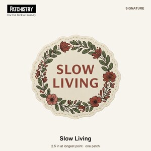 May include: A circular embroidered patch with a cream background and a scalloped edge. The text SLOW LIVING is centred in dark red. A wreath of green leaves and dark red flowers encircles the text. The patch measures 6.35 cm.