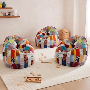 May include: Three bean bag chairs featuring a patchwork design made of various fabric squares in colours including red, blue, yellow, green, and white with diverse patterns. The chairs have a rounded, soft structure and are arranged on a rug.