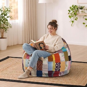May include: A patchwork beanbag chair in a room setting, with a person reading a book. The beanbag is made of various fabric squares in different colours. The person is wearing a cream sweater and blue jeans. A natural fibre rug is beneath.