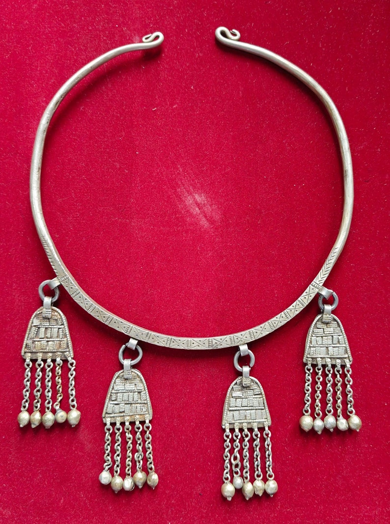 May include: A silver necklace with a wide band and three pendant charms. Each charm has a geometric design and a chain of silver beads.