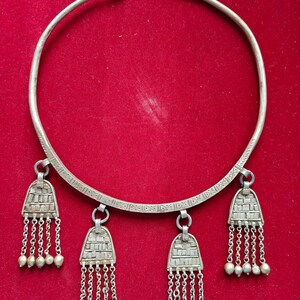 May include: A silver necklace with a wide band and three dangling pendants. Each pendant has a geometric design and a fringe of small silver beads.