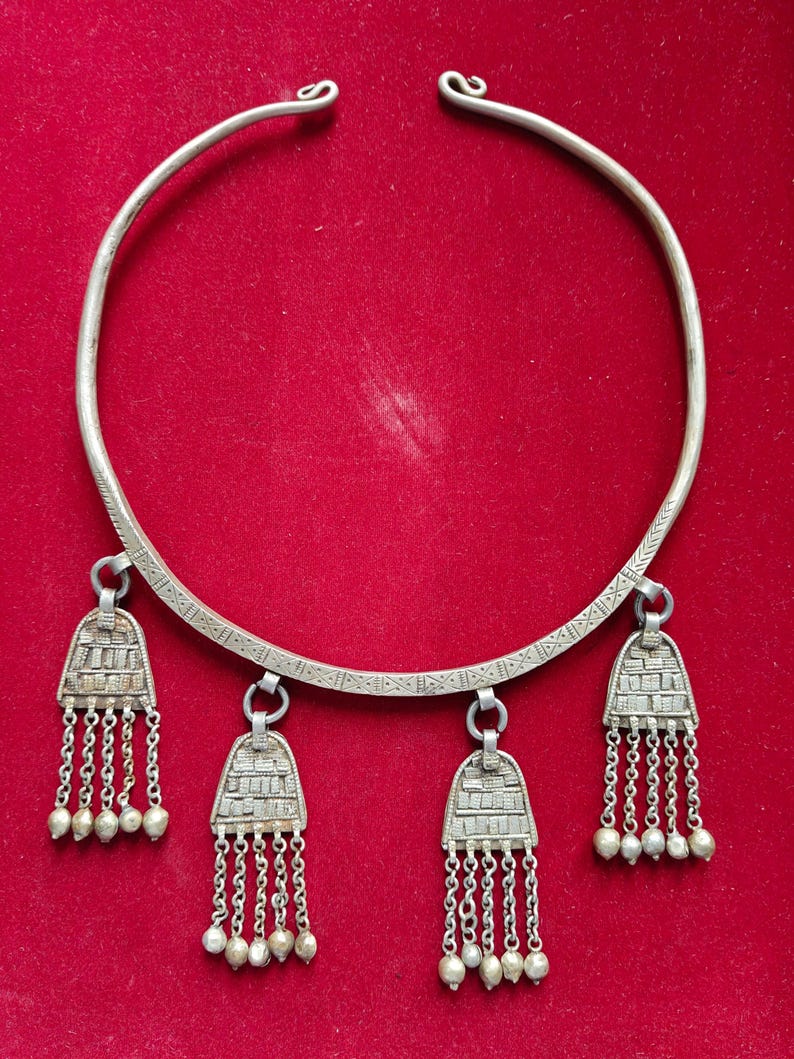 May include: A silver necklace with a wide band and three dangling pendants. Each pendant has a geometric design and a fringe of small silver beads.