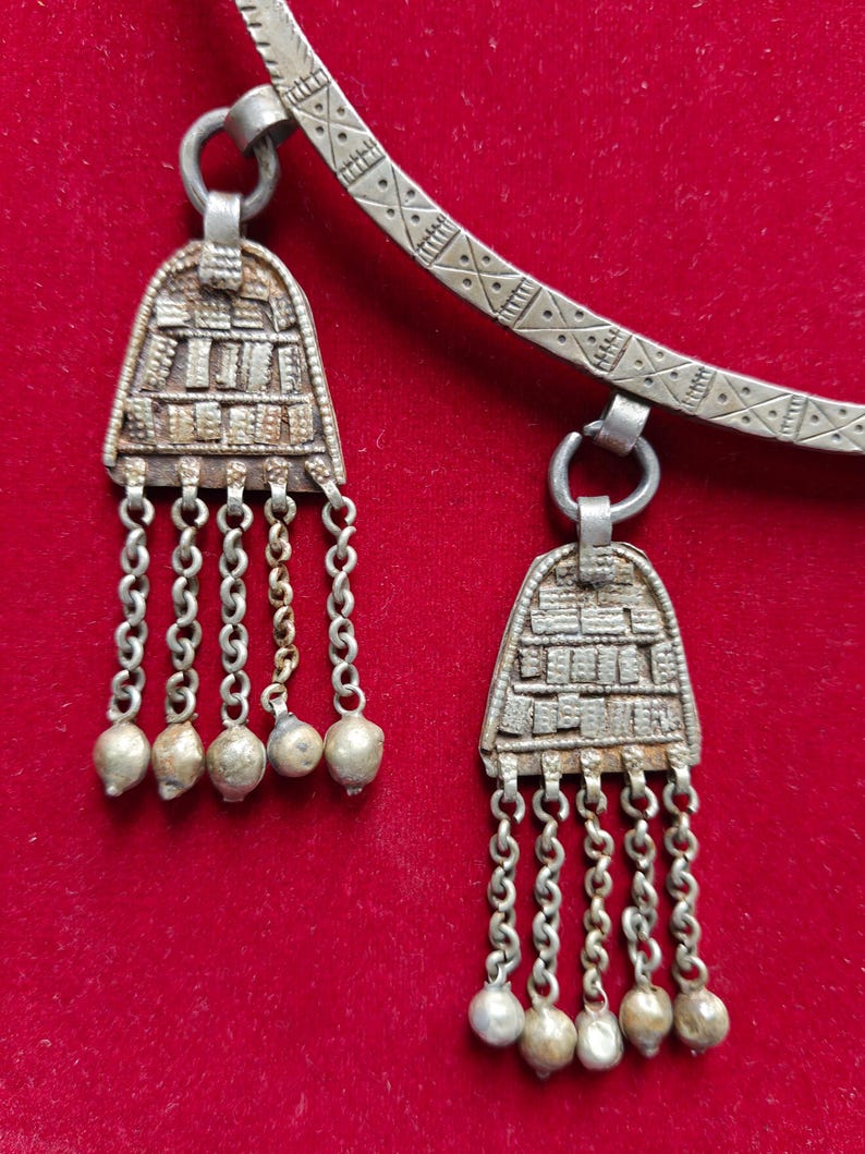May include: A silver necklace with two pendants. Each pendant has a geometric design and is attached to a chain with small silver beads.