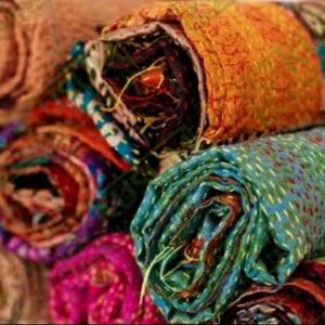 May include: Close-up of several rolled-up fabric pieces in various colors. The fabrics include shades of orange, teal, purple, and brown. The edges of the fabric are visible, revealing the layers and stitching details. The fabrics appear to be made of a textured material.