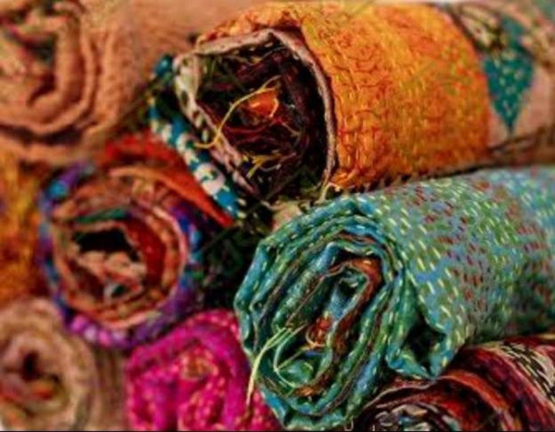 May include: Close-up of several rolled-up fabric pieces in various colors. The fabrics include shades of orange, teal, purple, and brown. The edges of the fabric are visible, revealing the layers and stitching details. The fabrics appear to be made of a textured material.