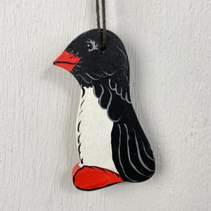 Peut inclure: Ornement de macareux marin en bois peint à la main. L'oiseau est noir et blanc avec un bec et des pieds rouges. Une ficelle marron est attachée pour l'accrocher. L'ornement est conçu pour ressembler à un macareux marin.