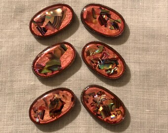 May include: Six oval-shaped buttons with a copper-colored metal frame and a pink iridescent background. The buttons are decorated with iridescent shell pieces.