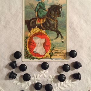 Puede incluir: Un anuncio vintage para el corsé Ball's Health Preserving, con una mujer a caballo. El anuncio está rodeado de 13 botones negros.