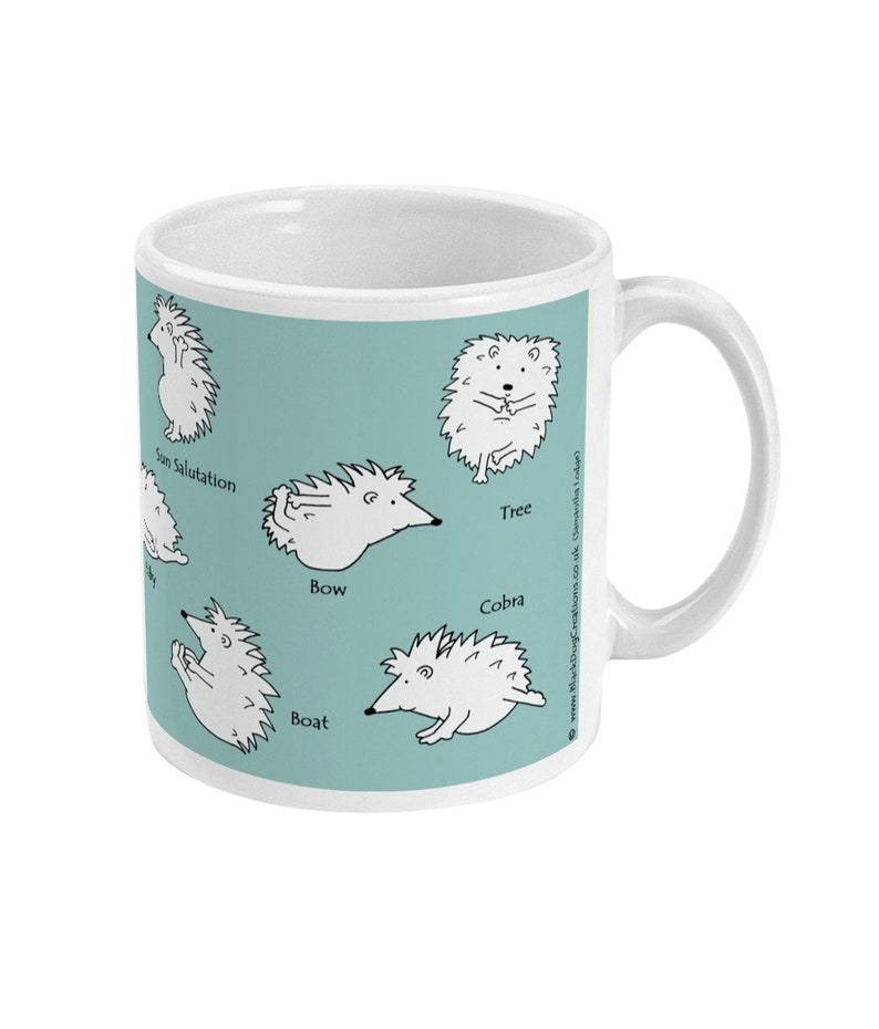 May include: White ceramic mug with a light teal background featuring cartoon hedgehogs in various yoga poses, including "Sun Salutation" and "Cobra". The mug has a white handle and a clean, modern design.