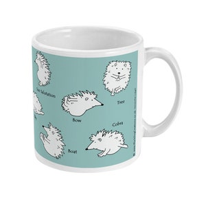 May include: White ceramic mug with a light teal background featuring cartoon hedgehogs in various yoga poses, including "Sun Salutation" and "Cobra". The mug has a white handle and a clean, modern design.
