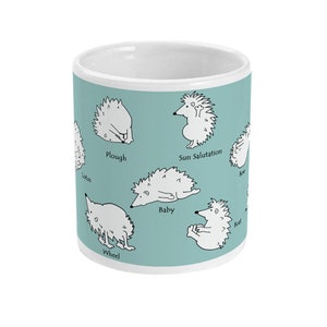 May include: White ceramic mug with a light teal background featuring cartoon hedgehogs in various yoga poses. Poses include Plough, Sun Salutation, and Boat. The mug has a white interior and a clean, modern design.