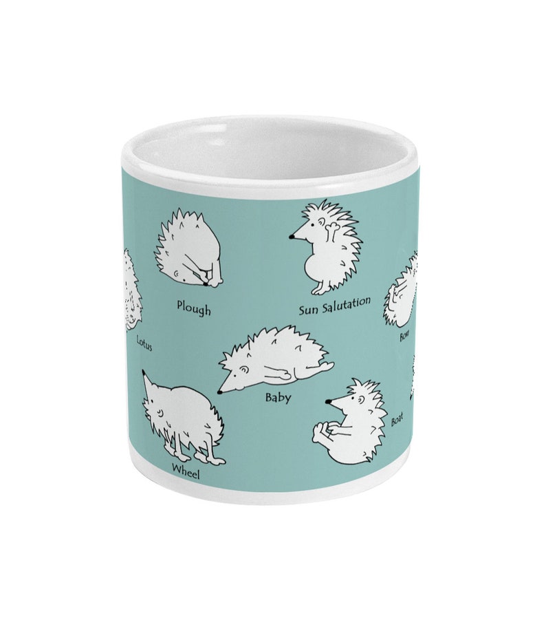 May include: White ceramic mug with a light teal background featuring cartoon hedgehogs in various yoga poses. Poses include Plough, Sun Salutation, and Boat. The mug has a white interior and a clean, modern design.