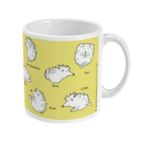 May include: White ceramic mug with a yellow background featuring cartoon hedgehogs in various yoga poses. Poses include Sun Salutation, Tree, Bow, Cobra, and Boat. The mug has a white handle and a white interior.