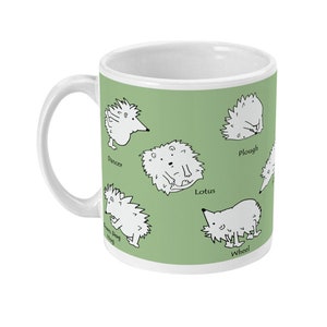 May include: White ceramic mug with a green background featuring cartoon hedgehogs in various poses. The mug has a white handle and the names "Dancer", "Lotus", "Wheel", "Plough", and "Town Dog Hog" are printed near the hedgehogs.