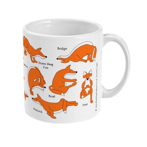May include: White ceramic mug with an orange fox in different yoga poses, including Down Dog Fox, Bridge, Boat, Tree, and Peacock. The text on the mug reads "Down Dog Fox", "Bridge", "Boat", "Tree", and "Peacock".