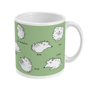 May include: White ceramic mug with a green background featuring cartoon hedgehogs demonstrating yoga poses. Poses include Sun Salutation, Tree, Bow, Boat, and Cobra. The mug has a white handle and a white interior.