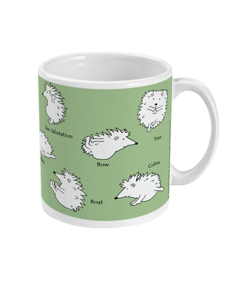 May include: White ceramic mug with a green background featuring cartoon hedgehogs demonstrating yoga poses. Poses include Sun Salutation, Tree, Bow, Boat, and Cobra. The mug has a white handle and a white interior.