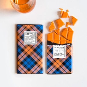 May include: Two chocolate bars with a plaid pattern and the text "SCOTTISH COLLECTION #015 [WHITE] IRON BREW & POPPING CANDY CHOCOLATE" on the front. One bar is broken into pieces and the pieces are scattered around the bar.