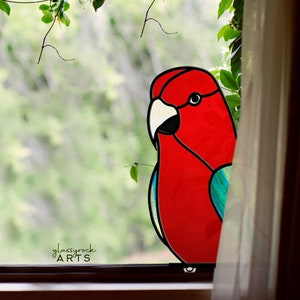 Peut inclure: Un perroquet en verre coloré avec des accents rouges, blancs et bleus est affiché dans une fenêtre. Le perroquet est tourné vers la gauche et est partiellement caché par un rideau blanc.