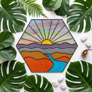 May include: A hexagonal stained glass panel featuring a landscape scene with a bright yellow sun rising over purple and grey mountains. Below the mountains are orange and brown hills with a blue river flowing through the centre of the composition.