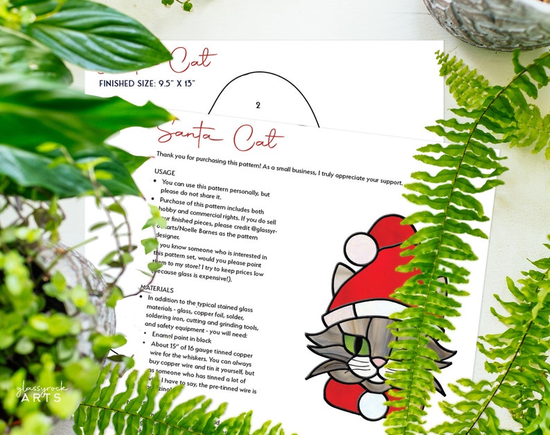 May include: A printed pattern for a stained glass Santa Cat, with a finished size of 9.5" x 13". The design features a gray cat wearing a red Santa hat. The pattern includes usage instructions and materials needed for the project.