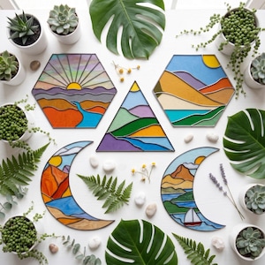 May include: Five stained glass suncatchers in geometric shapes including hexagons, a triangle, and two crescents. The designs feature colourful landscapes with mountains, rivers, suns, and a sailboat, all outlined in dark metal solder lines.