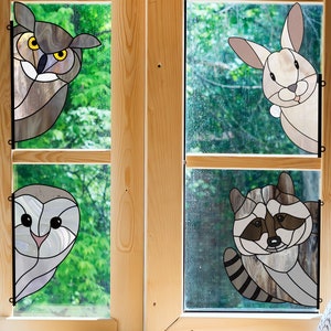 May include: Four stained glass panels depicting a brown owl, a white rabbit, a white owl, and a raccoon. The panels are framed in wood and set against a green leafy background.